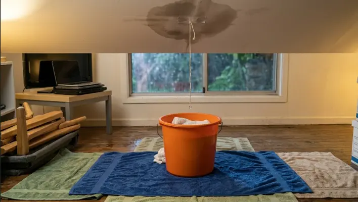 catch-and-contain-the-water A string is used to guide roof water into a bucket on a towel, illustrating a step-by-step method to catch and contain water from a ceiling leak.